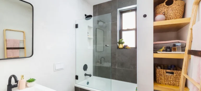 Small modern bathroom with bathtub, glass screen, wooden shelving, and black fixtures