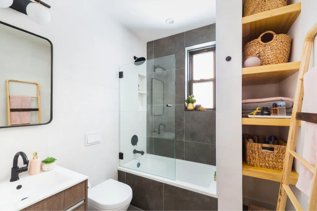 Small modern bathroom with bathtub, glass screen, wooden shelving, and black fixtures