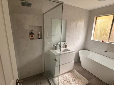 Frameless glass shower with full wall tiling and sleek white vanity in a Deakin Canberra bathroom